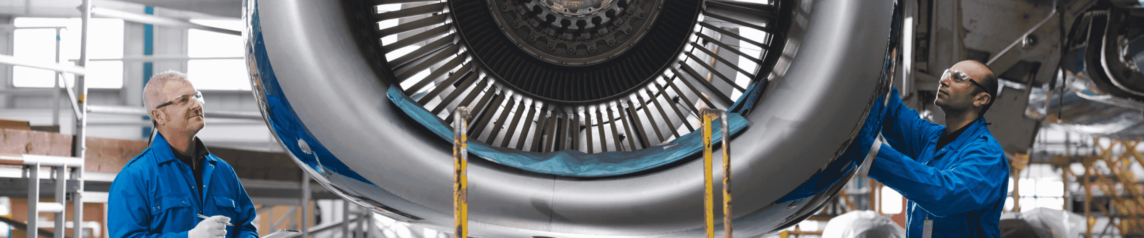 The picture show two inspectors closely observing an aircraft engine in a hangar.